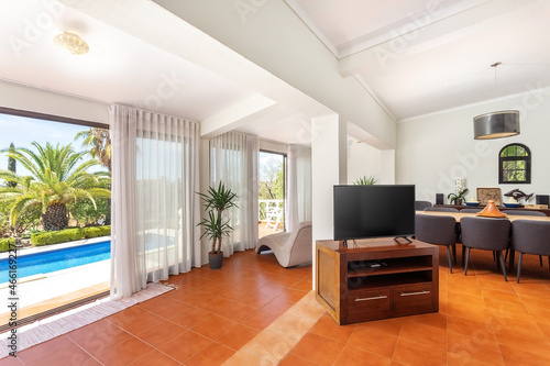 Modern traditional European living room with TV dinner table overlooking the pool and garden with palm trees.