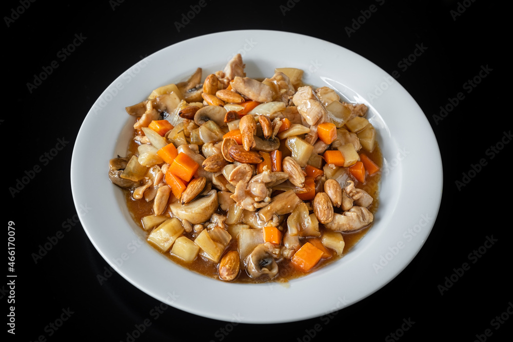 A traditional Chinese dish of chicken stew, with almonds, carrots and pasta. In a plate on a black background, close-up. A traditional Chinese dish of chicken stew, with almonds, carrots and pasta. In a plate on a black background, close-up.