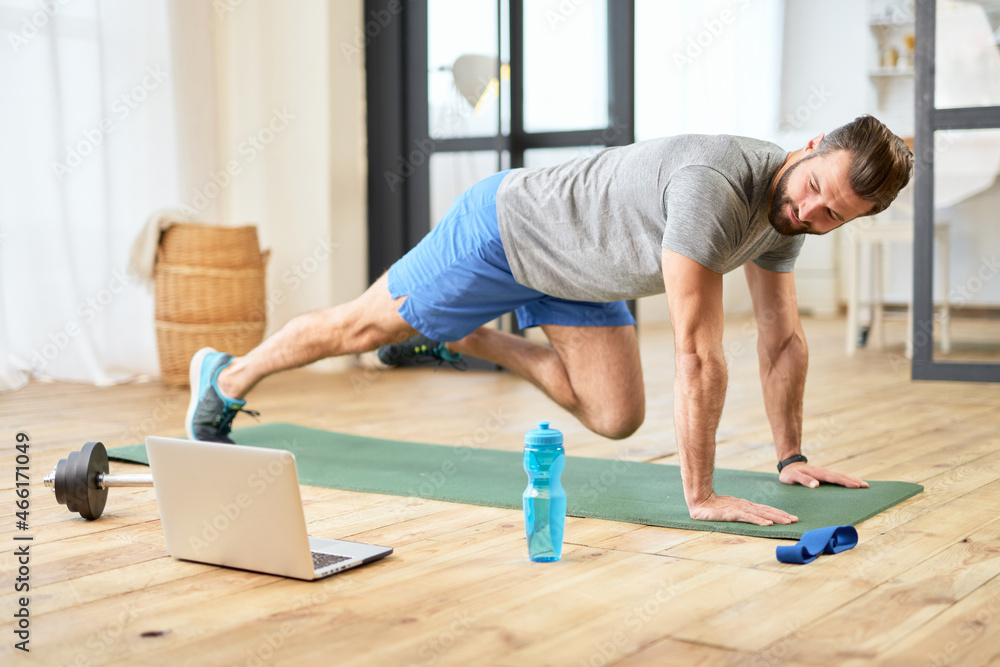 Bearded young man using notebook and working out at home Bearded young man using notebook and working out at home