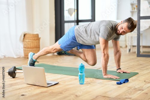 Bearded young man using notebook and working out at home