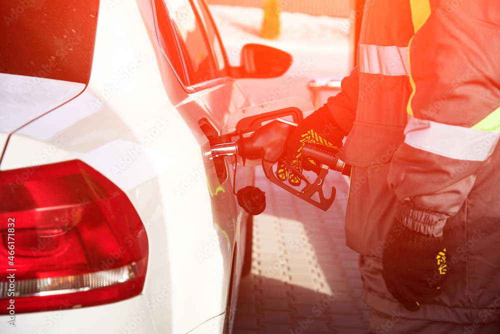 A gas station employee fills a car at a gas station with a hose from an oil column inserted in the tank on a sunny day.