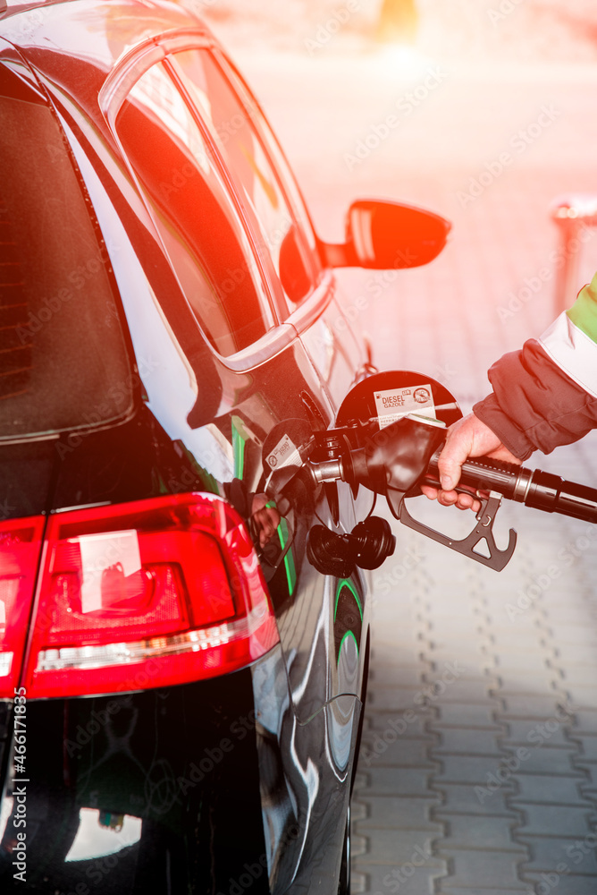 A man refueling a car at a gas station with a hose from an oil column inserted in the tank on a sunny day.