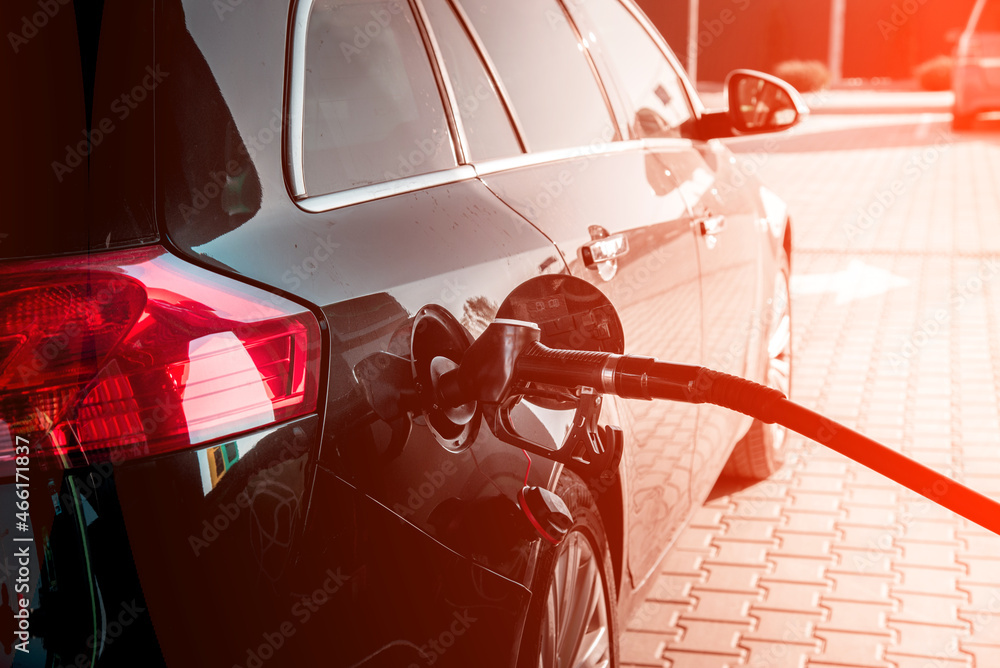 A car at a gas station with a hose from an oil column inserted in the tank on a sunny day.