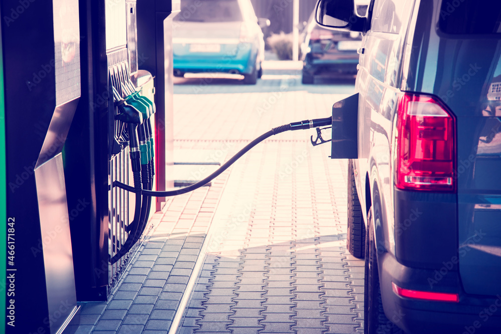 A car at a gas station with a hose from an oil column inserted in the tank. vintage style.