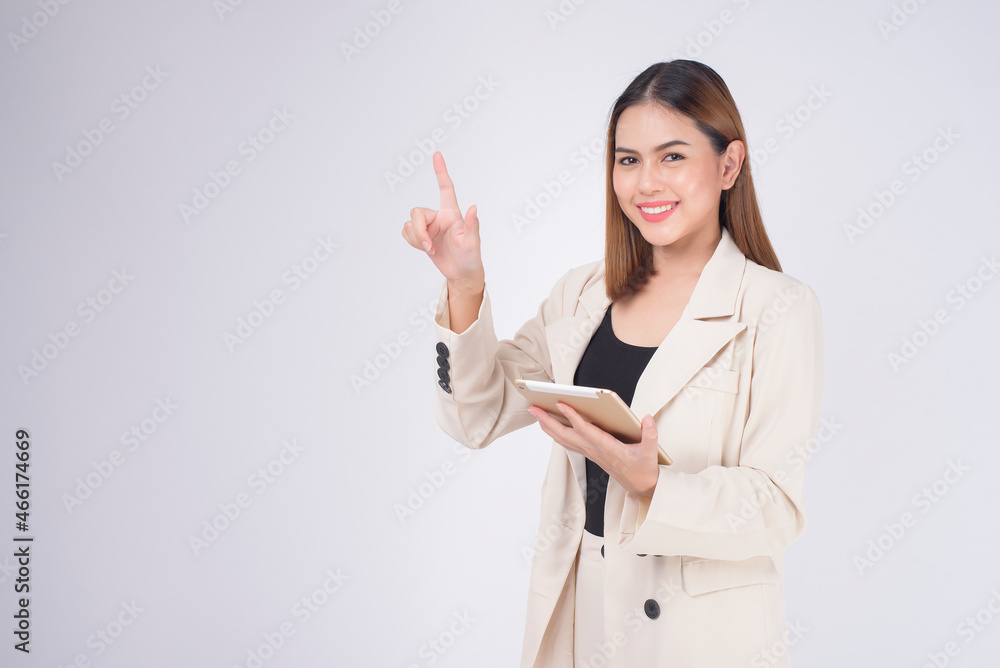 Young beautiful businesswoman in suit holding tablet over white Studio background.