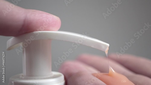 Pushing dispenser and liquid soap squeezed out to hand, closeup.