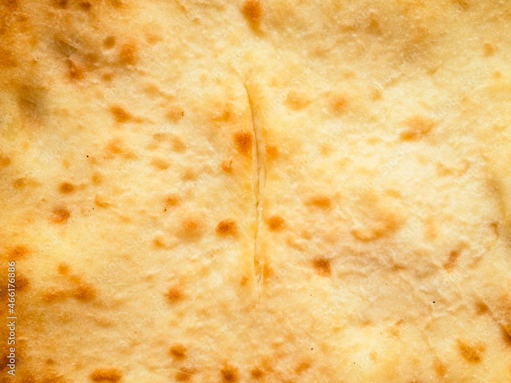 surface of flat closed pie Ossetian pie stuffed with cheese and potatoes close up