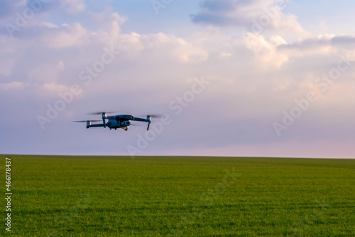 Drone hovers over a green field against a light sky. Summer drone flights. Drone patrols the fields.