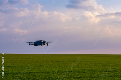 Drone hovers over a green field against a light sky. Summer drone flights. Drone patrols the fields.
