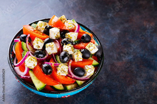 Greek salad in a bowl on a dark background. Healthy salad with feta cheese and olives. Fresh vegetable salad of Mediterranean cuisine. Copy space. Top view