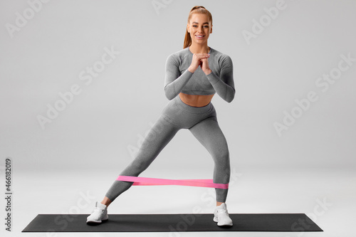 Fotografiet Athletic girl doing exercise for glutes with resistance band on gray background