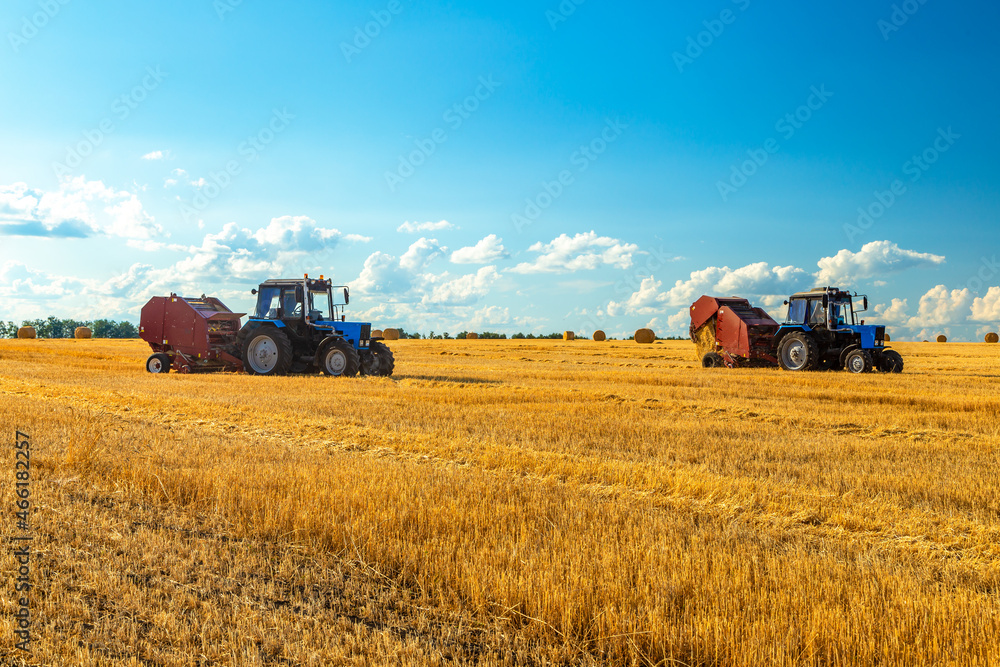 Fototapeta premium Bales of Hay in the Countryside and Tractor at Work in the background