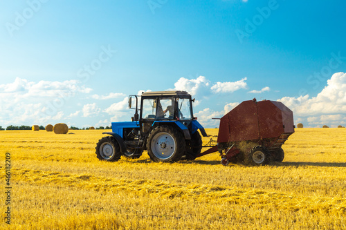 Tractor with bale machine for harvesting straw in the field and making large round bales. Agricultural work  harvesting hay on the hills in summer field