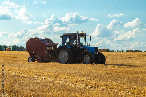 Tractor with bale machine for harvesting straw in the field and making large round bales. Agricultural work  harvesting hay on the hills in summer field