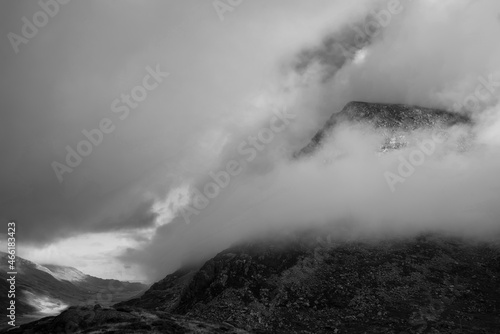 Black and white Epic mountain landscape image of Pen Yr Ole Wen in Snowdonia National Park with low cloud on peak and moodyfeel