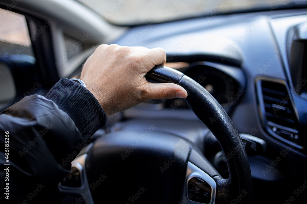 a man's hand holds the leather steering wheel of a car