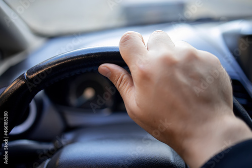 close-up of a man's hand holding the steering wheel of a car with two fingers