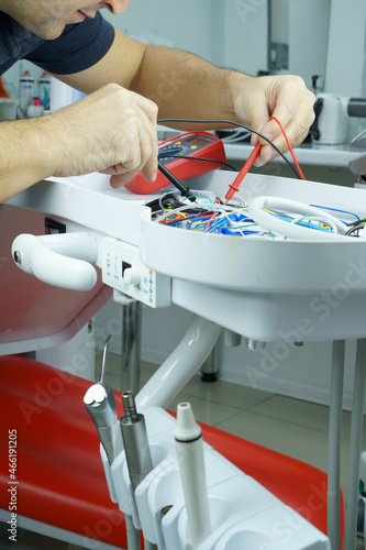 The master checks the electrical circuit in the faulty dental chair with a tester device. Repair of medical equipment.