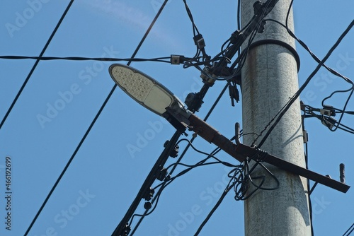 part of a gray concrete pillar with electrical wires and a lamp against the blue sky