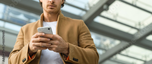 Photos Cropped view of smartphone in hands of blurred man in coat outdoors, banner