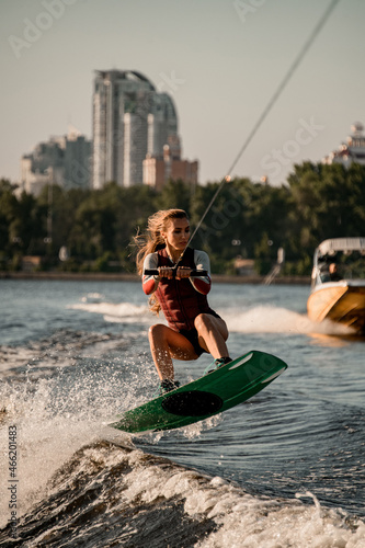 Beautiful active woman holds rope and jumping with wakeboard over river wave. photo