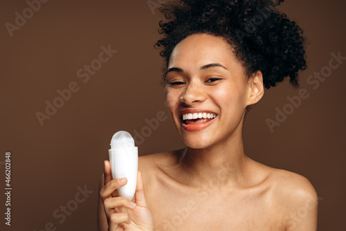 Outgoing multiracial woman preparing to applying antiperspirant on her body. Naked shoulders woman smiling toothy