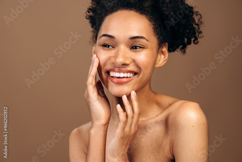 Face skin care. Woman applying cosmetic cream on clean hydrated skin portrait. Beautiful happy smiling multiracial girl model with natural makeup applying facial moisturizer. Beauty product concept