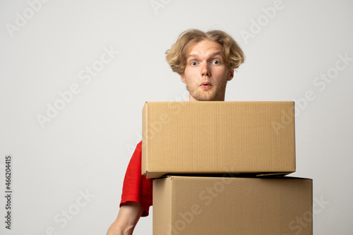 Cheerful delivery man. Happy young courier holding a cardboard boxes and smiling while standing against white background. Delivery man holding pile of cardboard boxes in front of himself. © Volodymyr