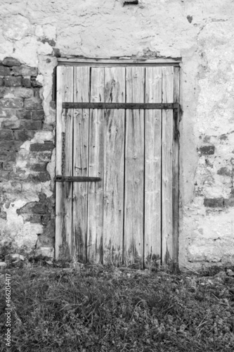 Stare drewniane drzwi z metalowymi zardzewiałymi okuciami w ścianie z cegły. Odpadający tynk ze ściany.