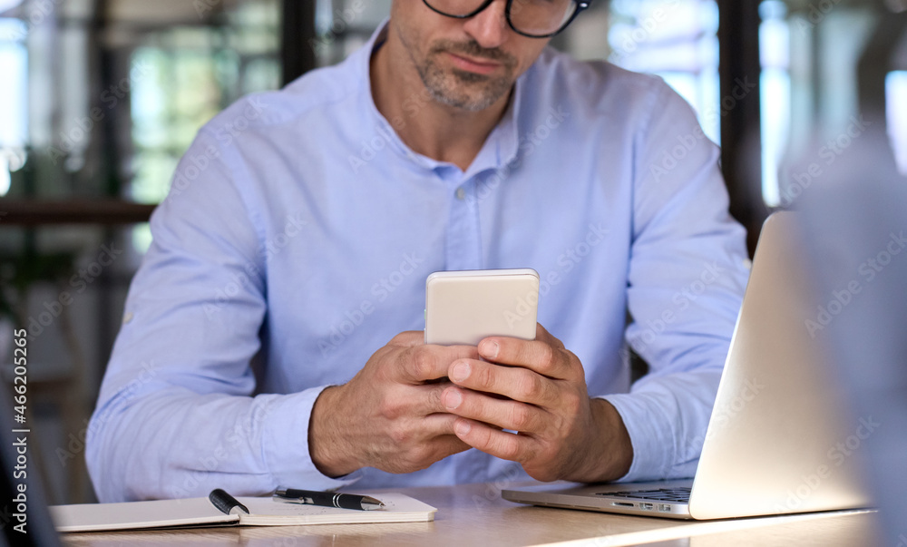 Close up of businessman holding using cell mobile smartphone in hands with laptop on desk in office. Technology applications for business development growth and solutions concept. Close up of businessman holding using cell mobile smartphone in hands with laptop on desk in office. Technology applications for business development growth and solutions concept.