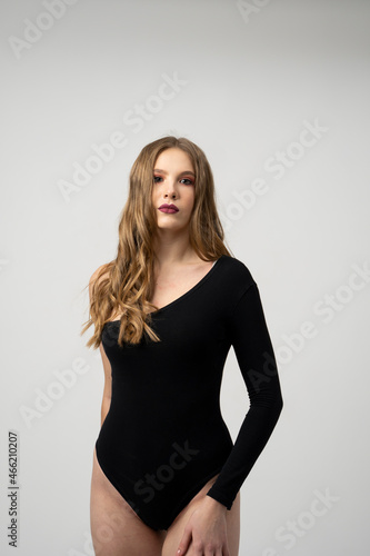 Beautiful young woman portrait in a black bodysuit. Studio shot, isolated on gray background. © Volodymyr