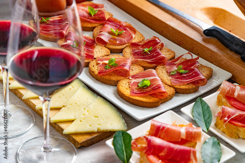 Aperitivos españoles. Aperitivos de jamón ibérico con una copa de vino, tomates maduros y queso de vaca sobre un fondo blanco de madera. photo