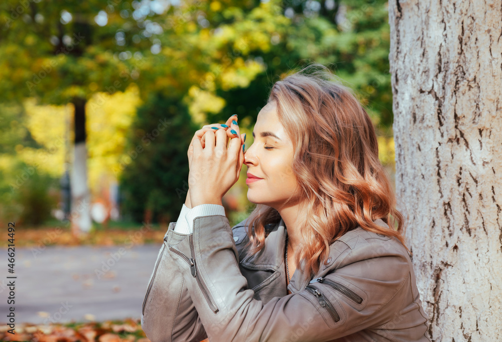 Portrait of a young dreamy woman in an autumn park. A young girl sits in the rays of sunlight with closed eyes under a tree in an autumn park. Portrait of a young dreamy woman in an autumn park. A young girl sits in the rays of sunlight with closed eyes under a tree in an autumn park.
