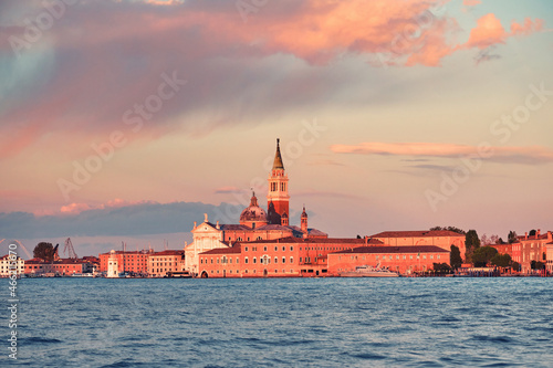 Church of San Giorgio Maggiore on San Giorgio island in Venice, Italy. Romantic Venetian architecture at sunset. Calm sea water and gorgeous orange and pink sunset clouds.