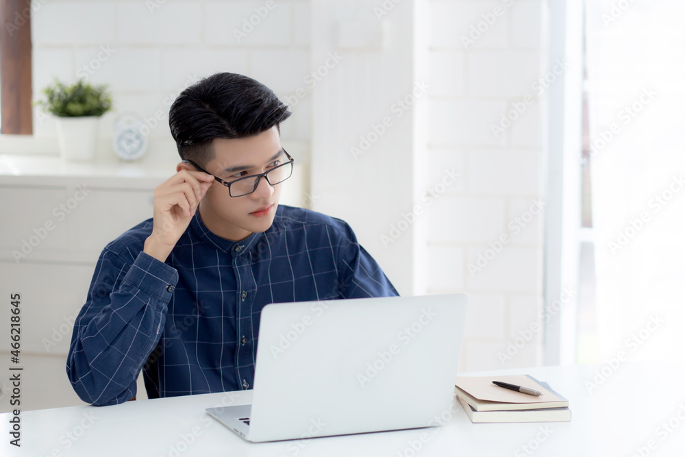 Young business man in glasses working from home with laptop computer on desk, freelance male sitting stay home using notebook for communication on table, entrepreneur in startup business, new normal. Young business man in glasses working from home with laptop computer on desk, freelance male sitting stay home using notebook for communication on table, entrepreneur in startup business, new normal.