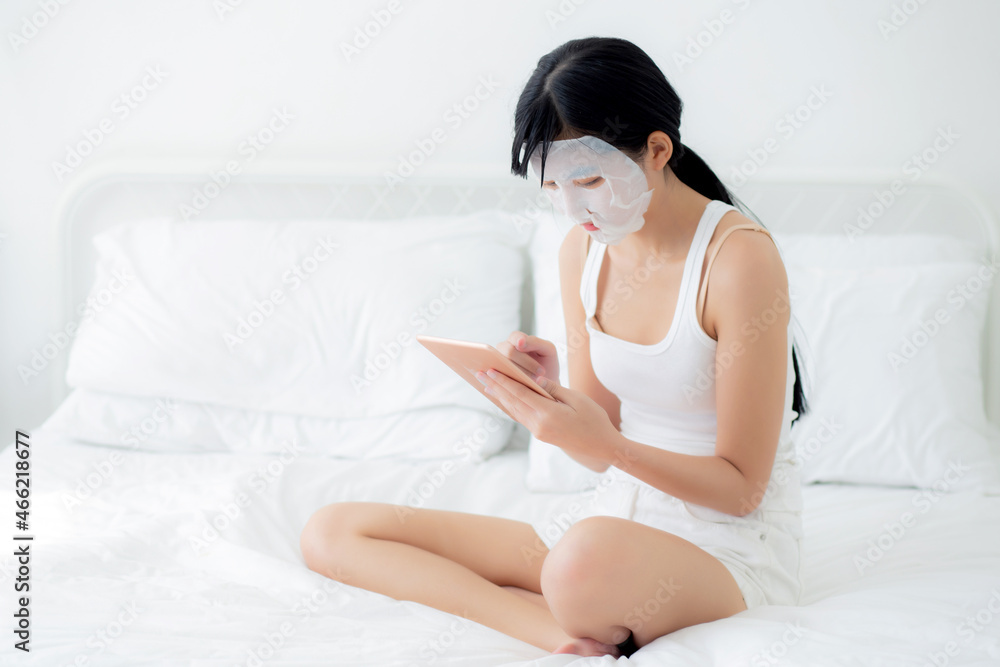 Beautiful young asian woman with sheet facial mask sitting watching tablet computer on bed at bedroom, beauty girl applying face mask for skincare of wrinkle at home, skin care, health and wellness. Beautiful young asian woman with sheet facial mask sitting watching tablet computer on bed at bedroom, beauty girl applying face mask for skincare of wrinkle at home, skin care, health and wellness.