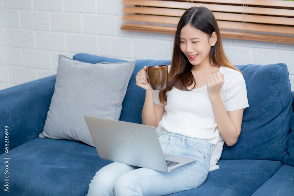 Young asian business woman smile and work from home with laptop computer online on sofa in living room, freelance girl using notebook and drink coffee on couch, new normal, lifestyle concept.