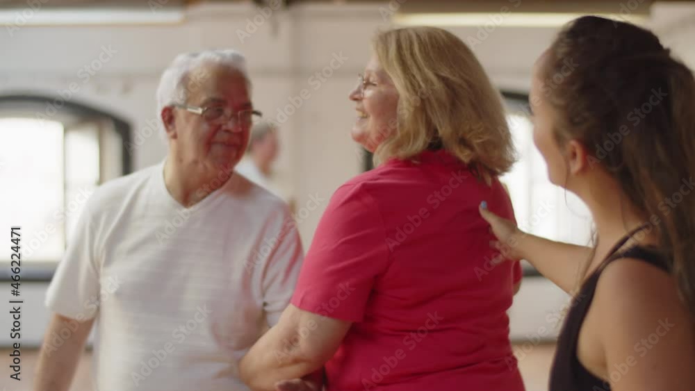 Medium shot of mature couple learning dance with instructor. Cute senior man and woman practicing movement to perfection in dance studio, swinging, holding each other elbow. Occupation, hobby concept Medium shot of mature couple learning dance with instructor. Cute senior man and woman practicing movement to perfection in dance studio, swinging, holding each other elbow. Occupation, hobby concept