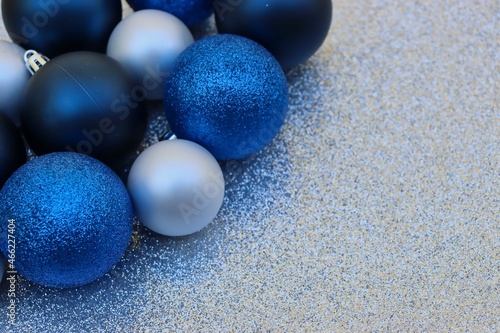 Closeup of blue and silver ornaments on silver glittery background with copy space.