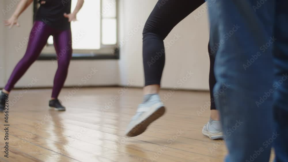 Close-up shot of group of people rehearsing dance combination. Men and women wearing sneakers and sportswear training in ballroom with teacher, learning movements. Dance class, fitness concept Close-up shot of group of people rehearsing dance combination. Men and women wearing sneakers and sportswear training in ballroom with teacher, learning movements. Dance class, fitness concept