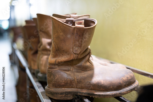 Row of dirty leather safety boots which is placed on the shoe rack. Industrial PPE equipment object, Close-up and selective focus.