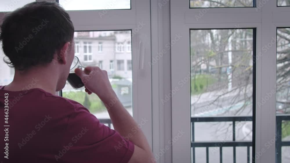 Man drinks coffee and watches through the window what is happening on the street Man drinks coffee and watches through the window what is happening on the street
