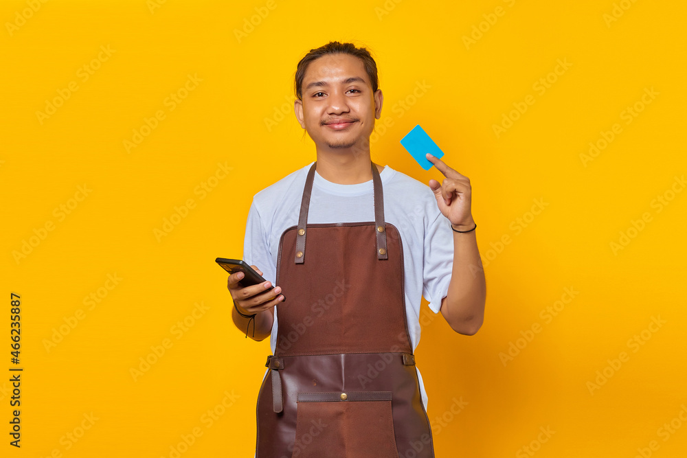 Portrait of smiling handsome barista showing credit card to pay and holding smartphone Portrait of smiling handsome barista showing credit card to pay and holding smartphone