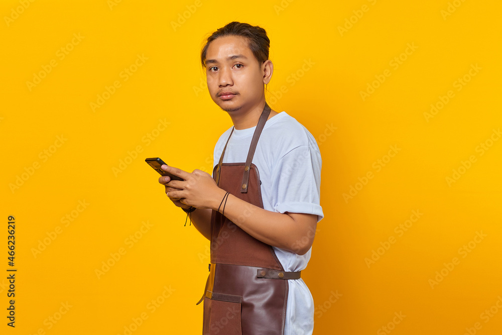 Portrait of happy Asian young man using smartphone and looking at front on yellow background Portrait of happy Asian young man using smartphone and looking at front on yellow background