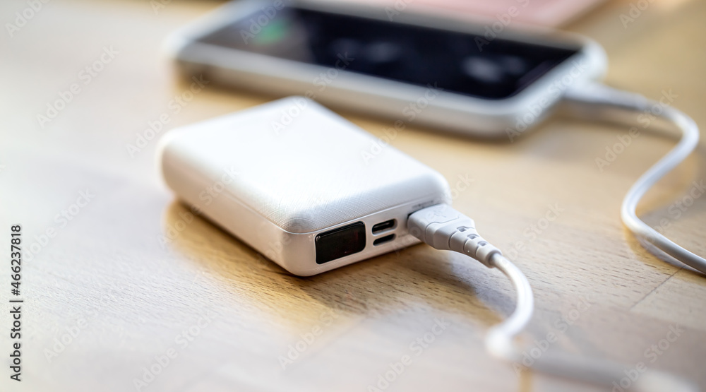 Fototapeta premium A smartphone is charged from a small white power bank.
