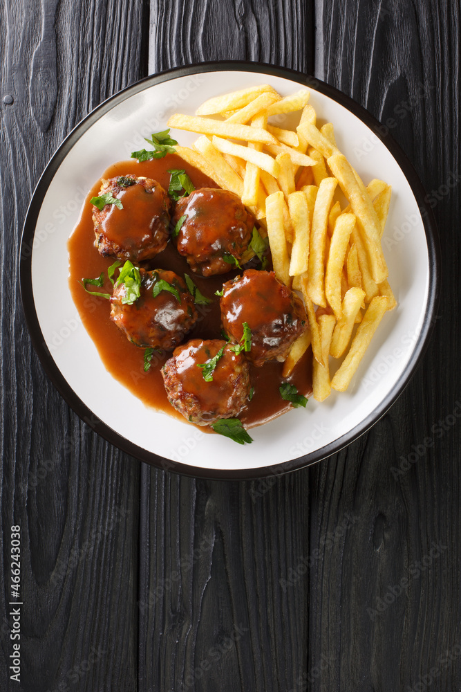 Boulets liegeois is a popular dish served all over Belgium made of meatballs swimming in an apple and onion gravy served with fries closeup in the plate on the table. Vertical top view from above Boulets liegeois is a popular dish served all over Belgium made of meatballs swimming in an apple and onion gravy served with fries closeup in the plate on the table. Vertical top view from above