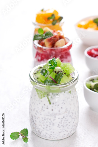 Chia pudding assortment with fruits and yogurt served in glass jars on the white table. Set of three healthy breakfast variations with kiwi, mango and figs