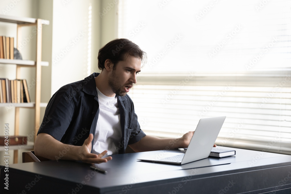 Confused angry young man looking at laptop screen, feeling anxious of made financial mistakes, irritated by bad gadget work, low internet connection, having problems working remotely at home office. Confused angry young man looking at laptop screen, feeling anxious of made financial mistakes, irritated by bad gadget work, low internet connection, having problems working remotely at home office.