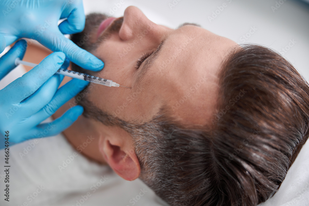 Skilled beautician does filler injection for crows feet to middle aged client in clinic Skilled beautician does filler injection for crows feet to middle aged client in clinic
