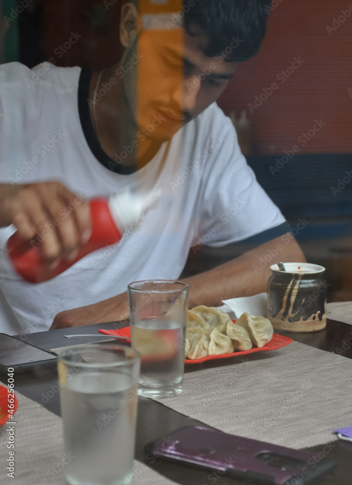 View of a young guy eating fast food in the cafe seen through the window glass. View of a young guy eating fast food in the cafe seen through the window glass.